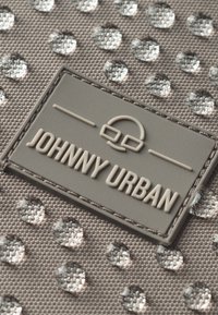 Gros plan sur un tissu texturé résistant à l'eau avec une étiquette en caoutchouc cousue affichant une icône de casque et le texte « Johnny Urban ». 