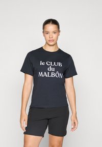 T-shirt in cotone nero con scritta bianca "le CLUB du MALBÔN." Maniche corte, vestibilità rilassata, abbinato a pantaloni corti neri attillati.
