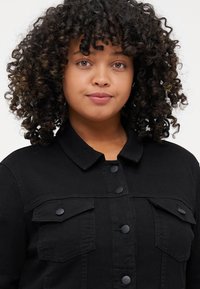 Black denim jacket with a collared neck, visible button closures, two chest pockets, and textured fabric, suitable for casual wear.