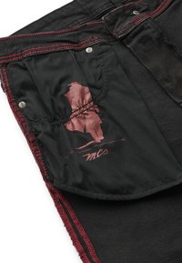 Țesătură din denim negru cu cusături roșii; prezintă o căptușeală a buzunarului neagră cu un grafic și logo cărămiziu. Viziune de aproape a detaliilor texturate.