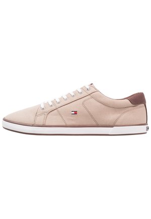 Baskets basses beiges avec lacets blancs, semelle blanche, accent marron au talon et petit logo rouge, blanc et bleu sur le côté.