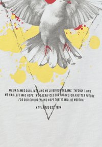 Paloma gris con garras rojas volando sobre manchas de pintura amarillas y un mensaje esperanzador sobre sueños y sacrificio, fechado en Key Largo 1994.