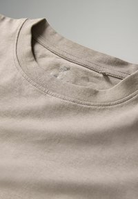 Ljust beige bomull t-shirt med rund halsringning. Mjuk textur med subtila sömsdetaljer och en etikett nära kragen.
