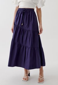 Gonna maxi a strati di colore blu navy realizzata in tessuto leggero, con una vita elastica dotata di cordoncino e dettagli in tonalità oro.