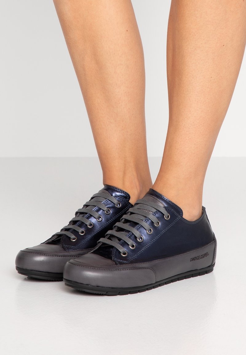 Baskets en cuir bleu marine avec des accents brillants, semelle en caoutchouc grise et lacets gris. Présentent un logo sur le côté et un design à bout rond.