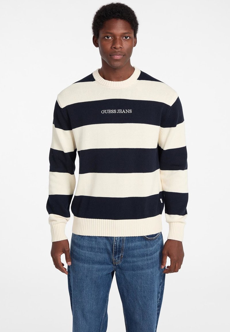Navy und creme gestreifter Pullover aus Strickstoff mit gerippten Bündchen und Saum, mit dem Logo "GUESS JEANS" auf der Vorderseite. Bequemer Schnitt.