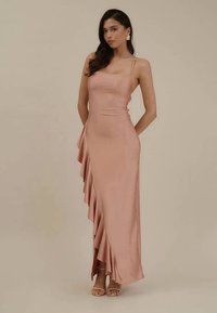 Vestido longo de cetim rosa com alças finas, apresentando um detalhe de babado drapeado ao longo do lado. Textura suave, design ajustado, silhueta até ao chão.