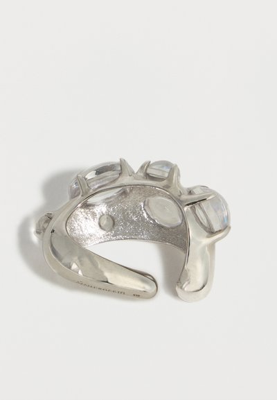 Ασημένιο βραχιόλι μανσέτα με πολλούς στρογγυλεμένους διαυγείς λίθους σε βραχίονες που μοιάζουν με τσιμπίδες, εμφανίζονται σε λευκό φόντο.