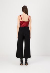 Camisón de satén rojo con tirantes ajustables, combinado con pantalones de pierna ancha negros de talle alto y botas de tacón negras.