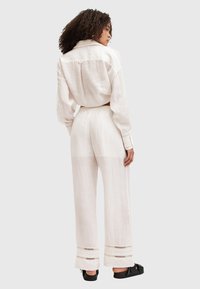 Linnen twee-delig outfit in off-white. Loszittend langwerpig shirt met kraag en wijde broek met kantaccenten aan de zoom.