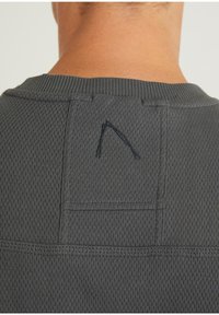 Top grigio con texture, dotato di un colletto a coste e un dettaglio del logo triangolare ricamato sul retro.