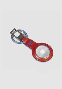 Rode leren sleutelhangerhouder met blauwe accenten, voorzien van een transparant rond vak voor een Apple-trackingapparaat en metalen beslag.