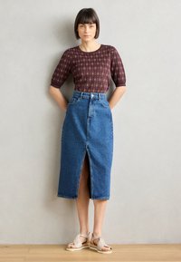Haut à motifs rouges avec des manches courtes, associé à une jupe midi en denim bleue taille haute avec une fente à l'avant. Des sandales beiges complètent le look.