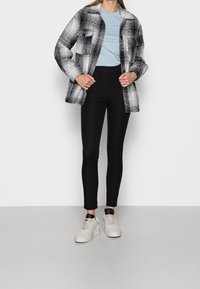 Svart och vit rutmönstrad skjortjacka över en ljusblå t-shirt, kombinerad med svarta leggings och beigefärgade sneakers med svarta detaljer.