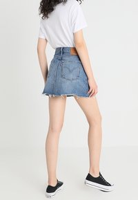 Minifalda de mezclilla de cintura alta, con dobladillo deshilachado y detalles de bolsillo trasero. Combinada con una camiseta blanca y zapatillas negras.