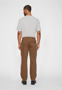 Grijs T-shirt met korte mouwen, losse pasvorm, gecombineerd met bruine cargobroek met zijzakken en een elastische tailleband. Zwarte schoenen maken de look compleet.