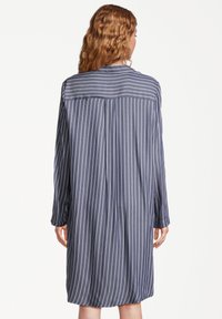 Abito camicia a righe blu navy con maniche lunghe, vestibilità rilassata e un'apertura sul retro. Presenta righe bianche verticali e una texture morbida.