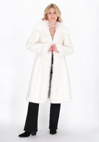 Long white coat with a fluffy fur collar and cuffs. Smooth texture, straight silhouette, and side pockets. Paired with black pants and boots.