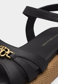 Μαύρο δερμάτινο πλατφόρμες σανδάλι με χρυσή αλυσίδα και ρυθμιζόμενο λουράκι στον αστράγαλο, διαθέτοντας πλεκτή υφή στη σόλα πλατφόρμας.