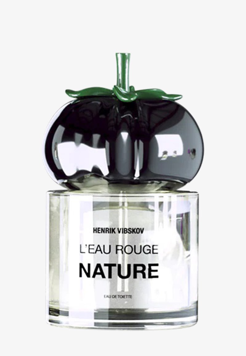 Svart glasflaska formad som en tomat, med en grön bladvip. Transparent bas med vit etikett med texten "Henrik Vibskov L’Eau Rouge Nature."