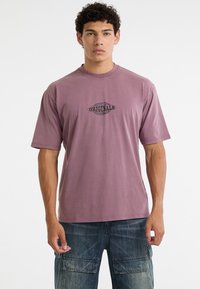 Korte mouwen t-shirt van zachte mauve katoen, met een zwart "ORIGINALS" logo gedrukt in het midden. Ontspannen pasvorm en ronde hals.