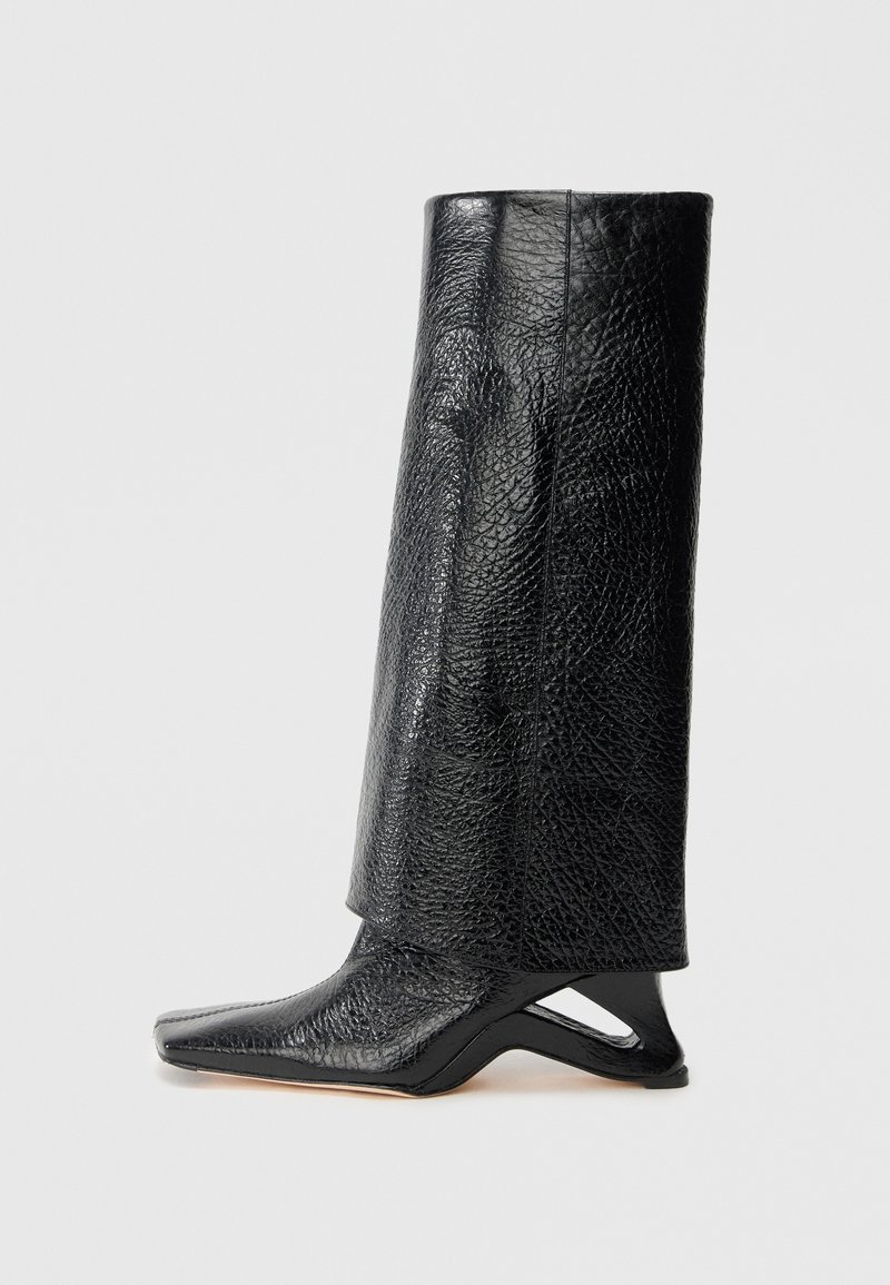 Čierna kožená čižma s textúrovaným povrchom, uhlovým strihom, špicatou špičkou a jedinečným dizajnom podpätku. Hladký povrch a dĺžka do polovice lýtok.
