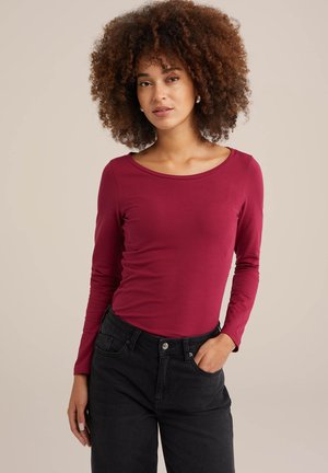 Langärmliges bordeauxfarbenes Oberteil aus einem weichen, elastischen Stoff mit Rundhalsausschnitt, kombiniert mit hochgeschnittenen schwarzen Jeans.