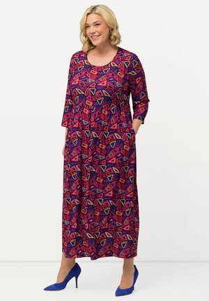 Robe longue colorée présentant des motifs géométriques vibrants en rose, violet et crème, avec des manches trois-quarts et des poches latérales.