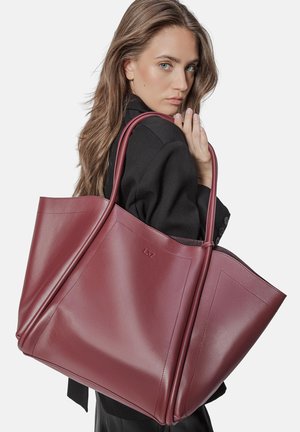 Burgundy leather tote bag with smooth texture, dual handles, and geometric design. Features a subtle embossed logo on one side.