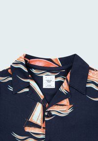 Camisa de manga corta en tejido azul marino con un estampado de veleros en naranja y azul claro, con cuello y un cierre de un solo botón.