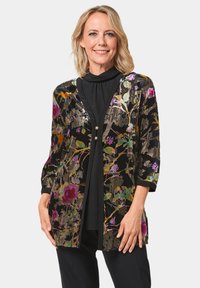 Schwarz gemusterte Jacke mit floralem Design und metallischen Akzenten, mit Dreiviertelärmeln, zwei vorderen Knöpfen und einem lockeren Schnitt über einem schwarzen Oberteil.