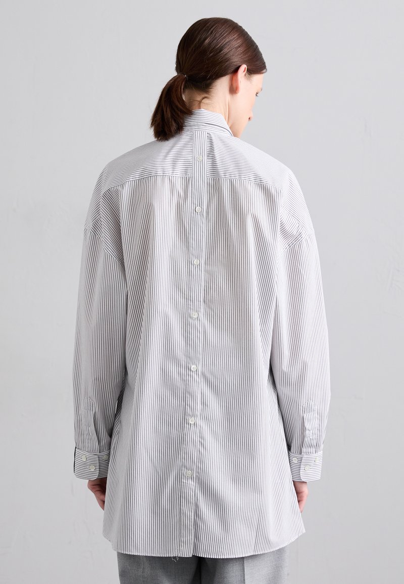 Chemise à rayures en mélange de coton ; présente un col haut, un dos allongé et des boutons au centre avec des manches longues.