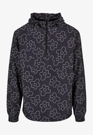 Melna vējjakas virsotne ar baltu ziedu rakstu, pus-izvilkšana priekšā, regulējama kapuce un elastīgi aproces. Gluda, viegla auduma.