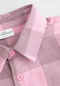 Różowo-szara koszula w kratkę z guziczkami, posiadająca spiczasty kołnierzyk i różowe guziki, wykonana z miękkiego, teksturowanego materiału. Widoczna metka z informacjami o rozmiarze.