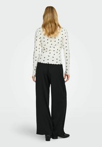 Biała bluzka z długim rękawem w czarny kwiatowy wzór, zestawiona z szerokimi czarnymi spodniami. Bluzka ma falbaniasty dół. Gładka tekstura i dopasowany krój.