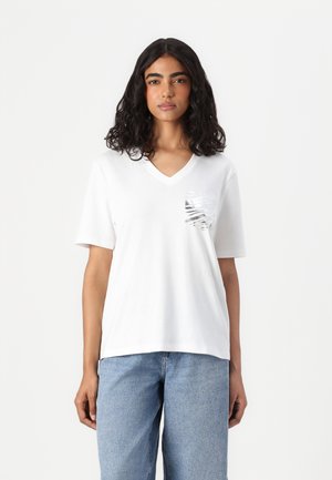 White short-sleeve V-neck T-shirt made of cotton, featuring a textured, shiny pocket design. Worn with light blue denim jeans.