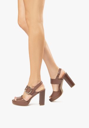 Sandali platform marroni con tacco grosso, punta aperta e dettaglio con fibbia. Materiale in pelle liscia con un accento cucito sul tacco.