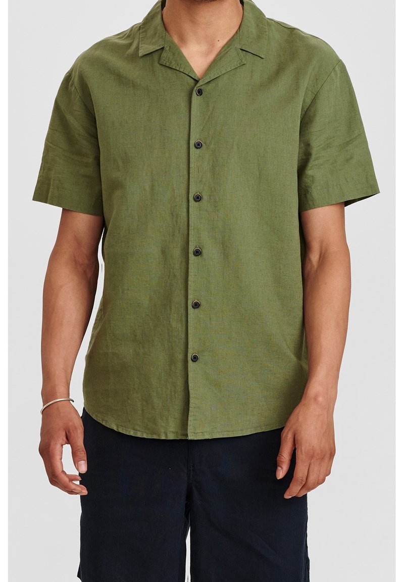 Camicia verde a maniche corte con bottoni, realizzata in tessuto texturizzato, dotata di colletto a punta e sei bottoni neri sulla parte anteriore.