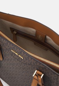 Bruine monogram tas met een ritsvak, gouden hardware-accenten en taupe voering. Beschikt over dubbele handvatten en een merkinterieur.