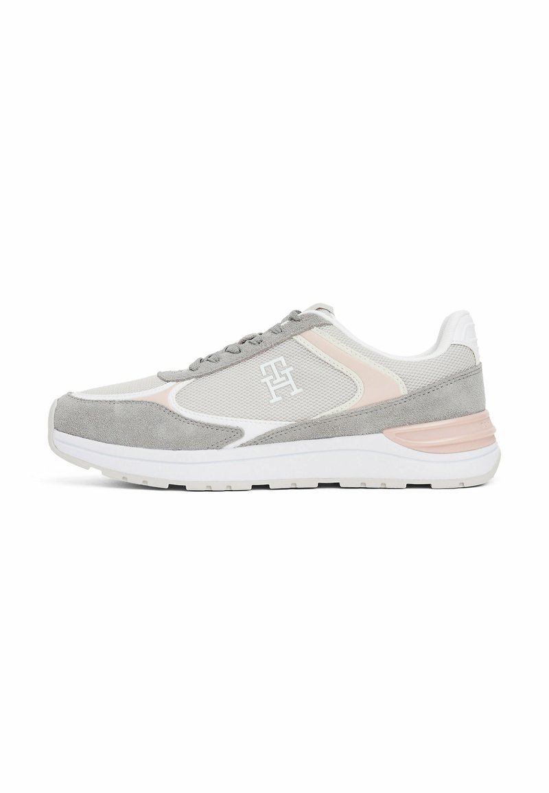 Chaussure de sport grise et blanche en matériaux daim et mesh, design à lacets, accents roses et semelle texturée. Logo présent sur le côté.