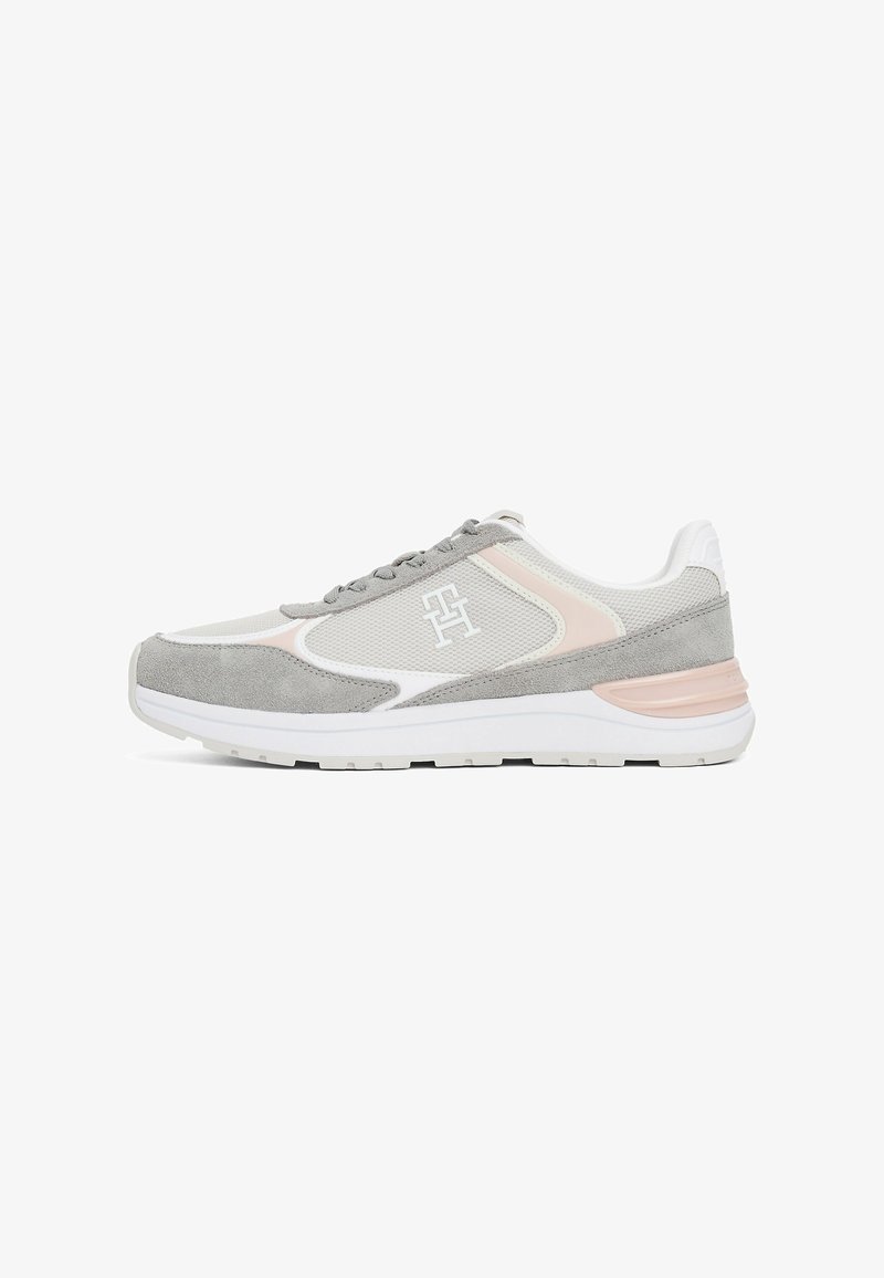 Chaussure de sport grise et blanche en matériaux daim et mesh, design à lacets, accents roses et semelle texturée. Logo présent sur le côté.