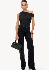 Body noir à une épaule, jeans noirs taille haute et sac à main noir avec des accents dorés. La mannequin porte des boucles d'oreilles créoles et des talons brillants.