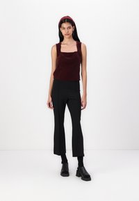 Bordo plišani top bez rukava sa kvadratnim izrezom, uparen s crnim širokim hlačama i masivnim crnim sandalama na petu. Jednostavan, elegantan dizajn.