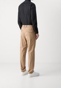 Černá tričko s dlouhým rukávem ve spojení s khaki kalhotami s elastickým pasem a bílými teniskami, vybavené zadními kapsami a volným střihem.