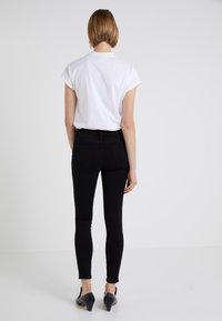 Camiseta blanca de manga corta, jeans ajustados negros y zapatos de tacón negros. Textura de tela suave, corte ceñido y diseño minimalista.