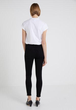 Camiseta blanca de manga corta, jeans ajustados negros y zapatos de tacón negros. Textura de tela suave, corte ceñido y diseño minimalista.