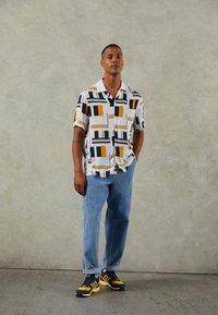 Kortärmad skjorta med knappar i ett geometriskt mönster i vitt, blått och orange. Kombinerad med ljusblå jeans och marinblå sneakers.