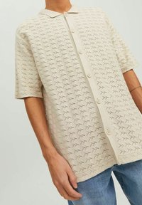 Beige polo shirt met korte mouwen, gekenmerkt door een gestructureerde, patroonstof, een klassieke kraag en een knoopsluiting aan de voorkant.