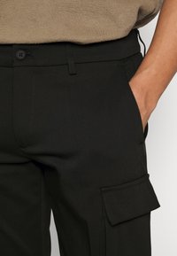 Sorte cargo-bukser lavet af glat, let stof; har en frontlomme og en sidelomme med flap; inkluderer en knaplukning.