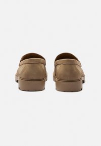 Barna bőr slip-on cipők sima textúrával, kerek orral és gumitalppal; minimális varrással és alacsony sarokkal rendelkeznek.
